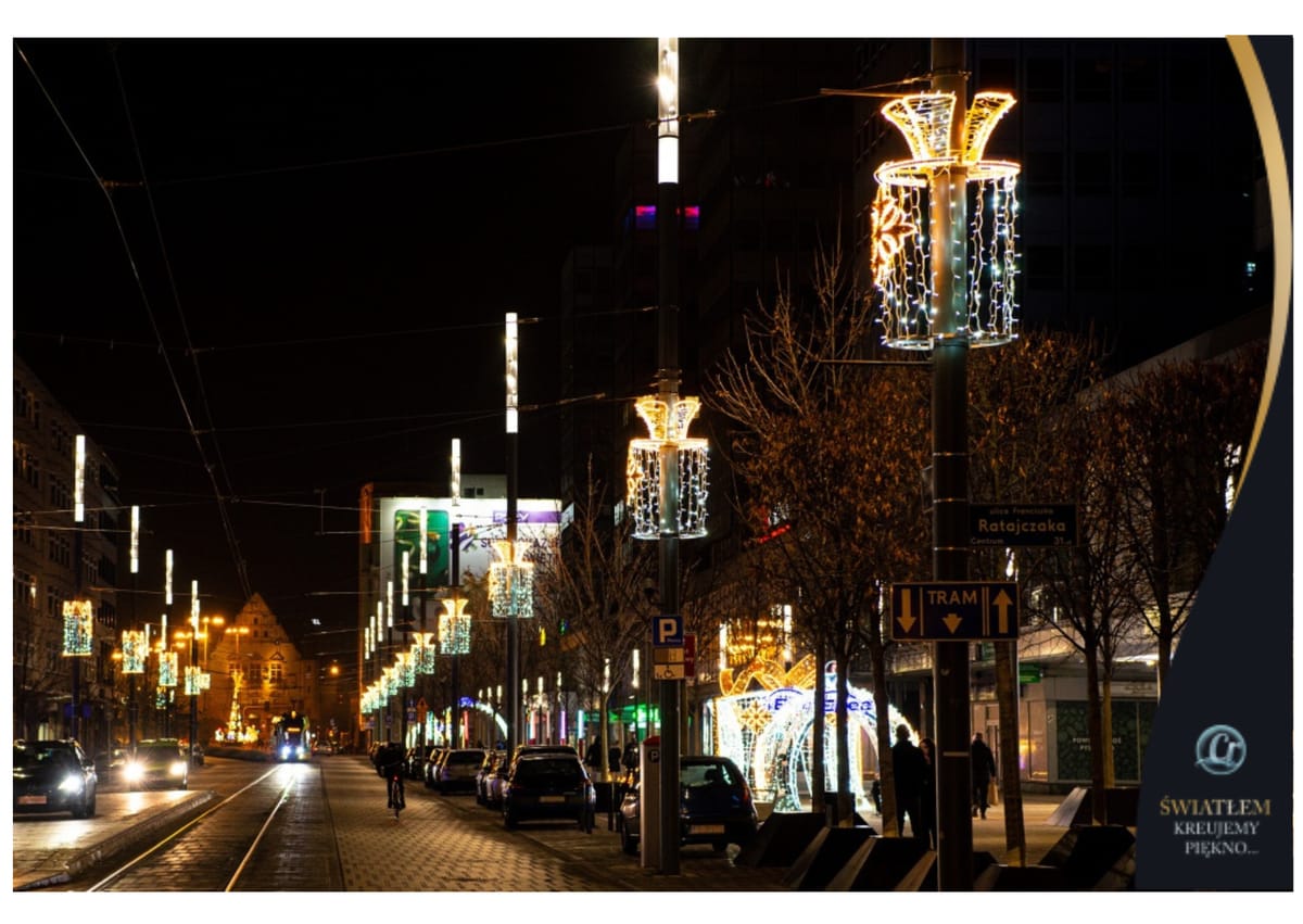 Nocna ulica z szeregiem rozświetlonych dekoracji na latarniach, po środku torowisko tramwajowe